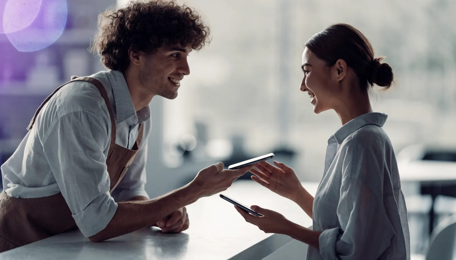 A team member offering their phone to a customer at the counter so they can scan and leave a review